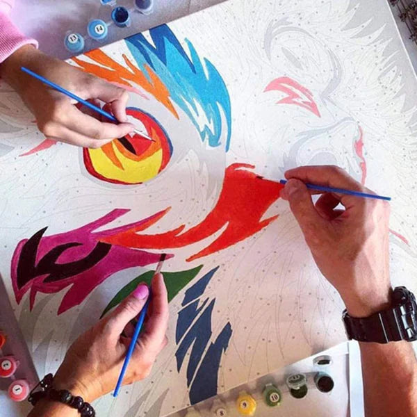 Person painting colorful abstract designs on a white surface with blue paintbrushes.